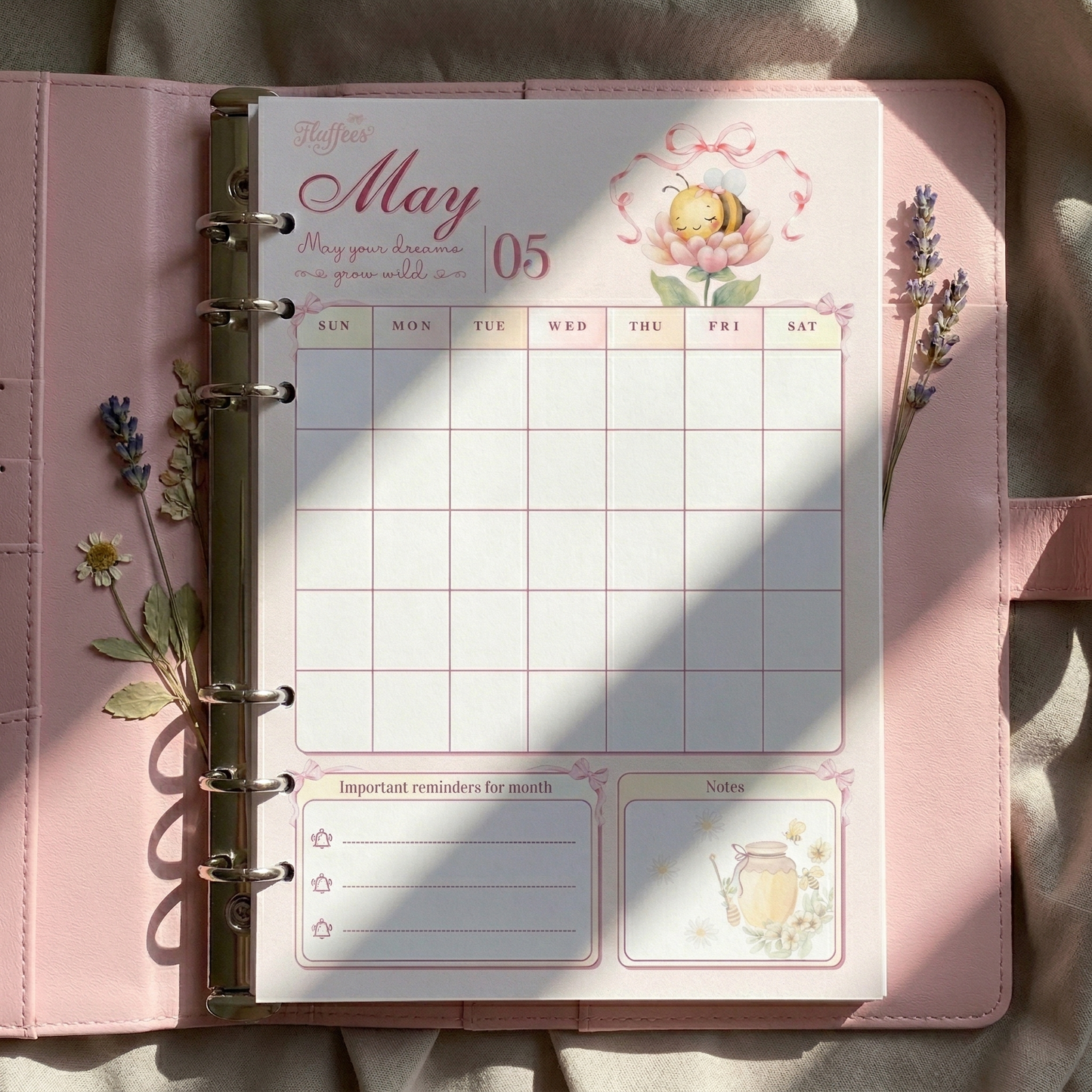 Pink planner with a floral design on a light brown surface with may calendar