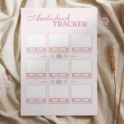 Lifestyle mockup of the audiobook tracker printed on premium paper, styled on a neutral fabric with rustic wheat stalks and checkered buttons. The scene highlights the cozy, aesthetic feel of this printable bullet journal page for book lovers.
