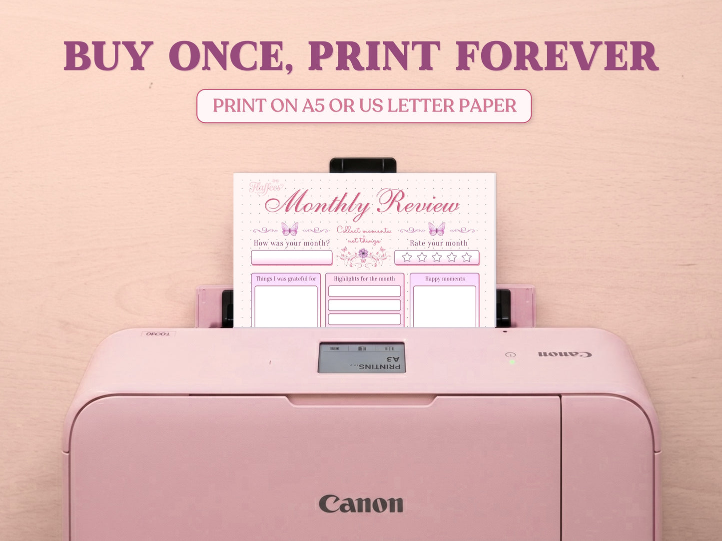 A printable monthly review page being printed from a pastel pink Canon printer on a light wood desk setup. The image template includes large decorative text saying 'BUY ONCE, PRINT FOREVER' and 'PRINT ON A5 OR US LETTER PAPER' to highlight its printable features for a bullet journal.