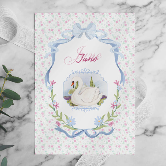 A video flip-through of the June Bullet Journal pages placed on a white marble table. The video showcases various layouts including the swan cover, habit trackers, and workout challenges in a soft pink aesthetic. Surrounded by decorative elements like eucalyptus, lace, and pearls in bright, natural light.